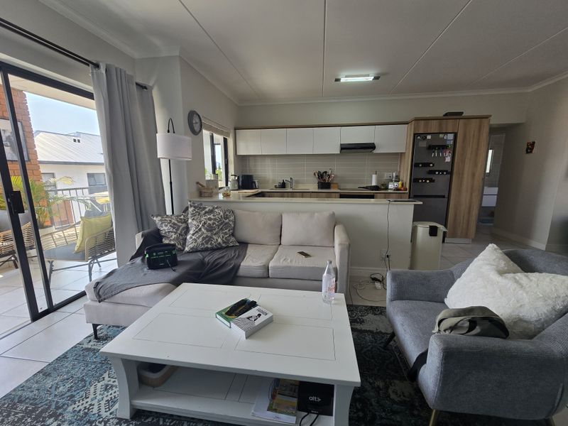 Open-plan living area featuring a modern kitchen with built-in cabinetry and a breakfast counter, seamlessly flowing to a private balcony through sliding glass doors.