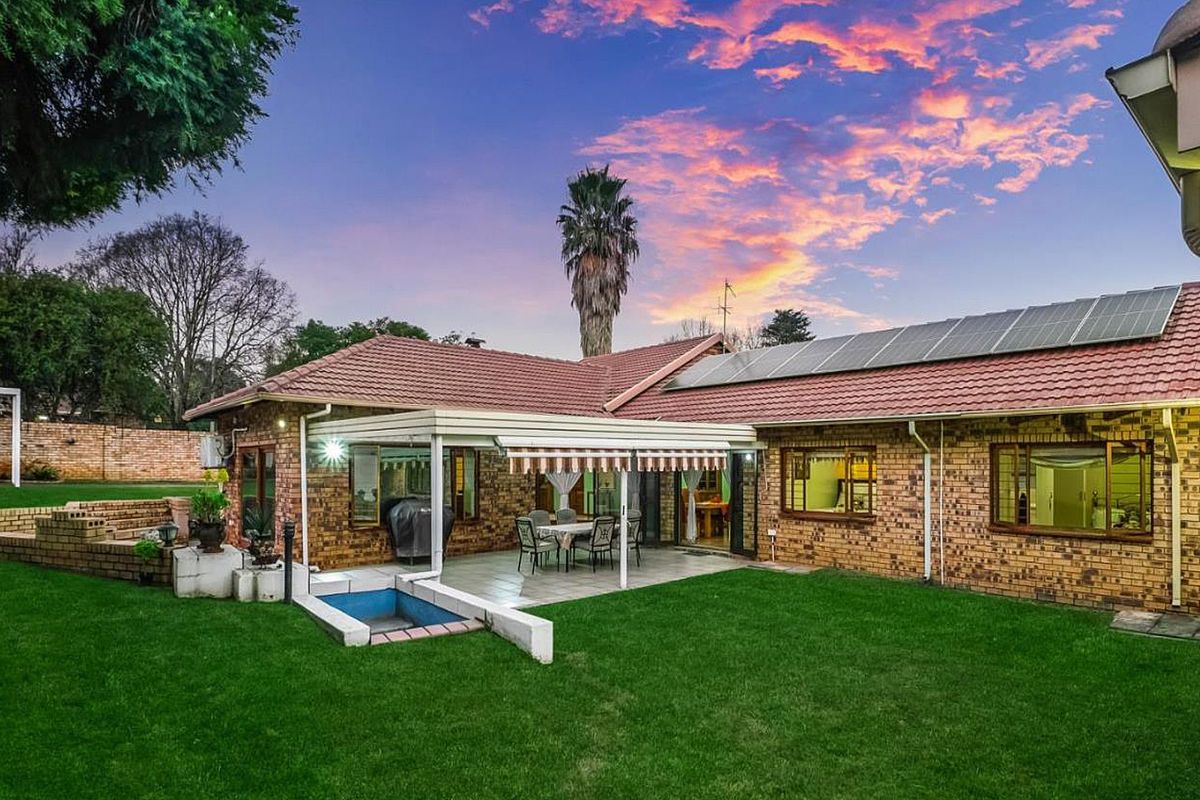 Rear view of a brick house featuring a covered patio, small plunge pool, solar panels on the roof, and a well-maintained garden.