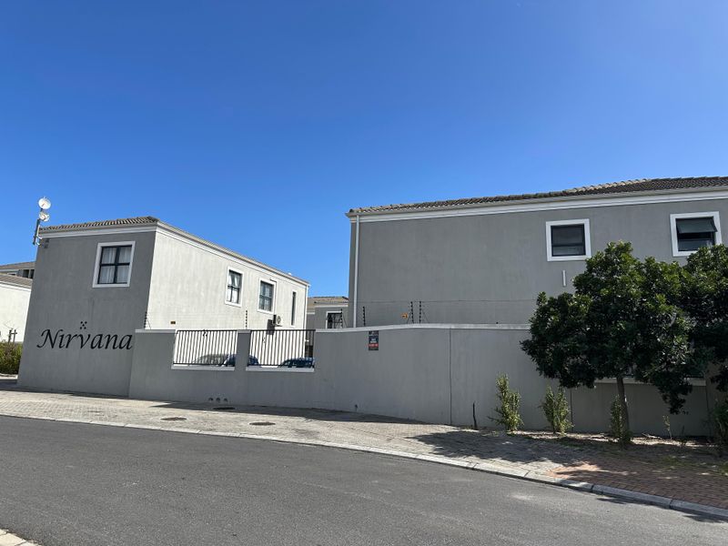 Front exterior view of the Nirvana townhouse complex, featuring grey rendered facades, tiled roofing, and secure boundary walls with electric fencing.
