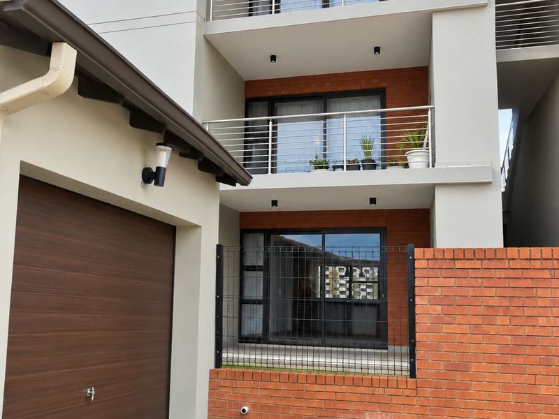 Modern multi-story apartment exterior featuring a paved driveway, integrated garage, brick facade accents, and private balconies with stainless steel railings.