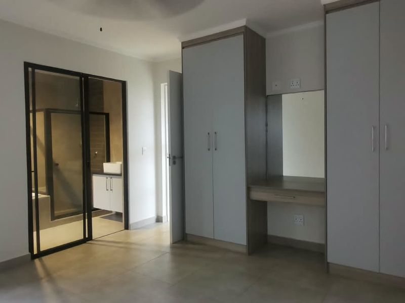 Spacious bedroom featuring modern built-in cupboards, a vanity station, tiled flooring, and direct access to an en-suite bathroom.