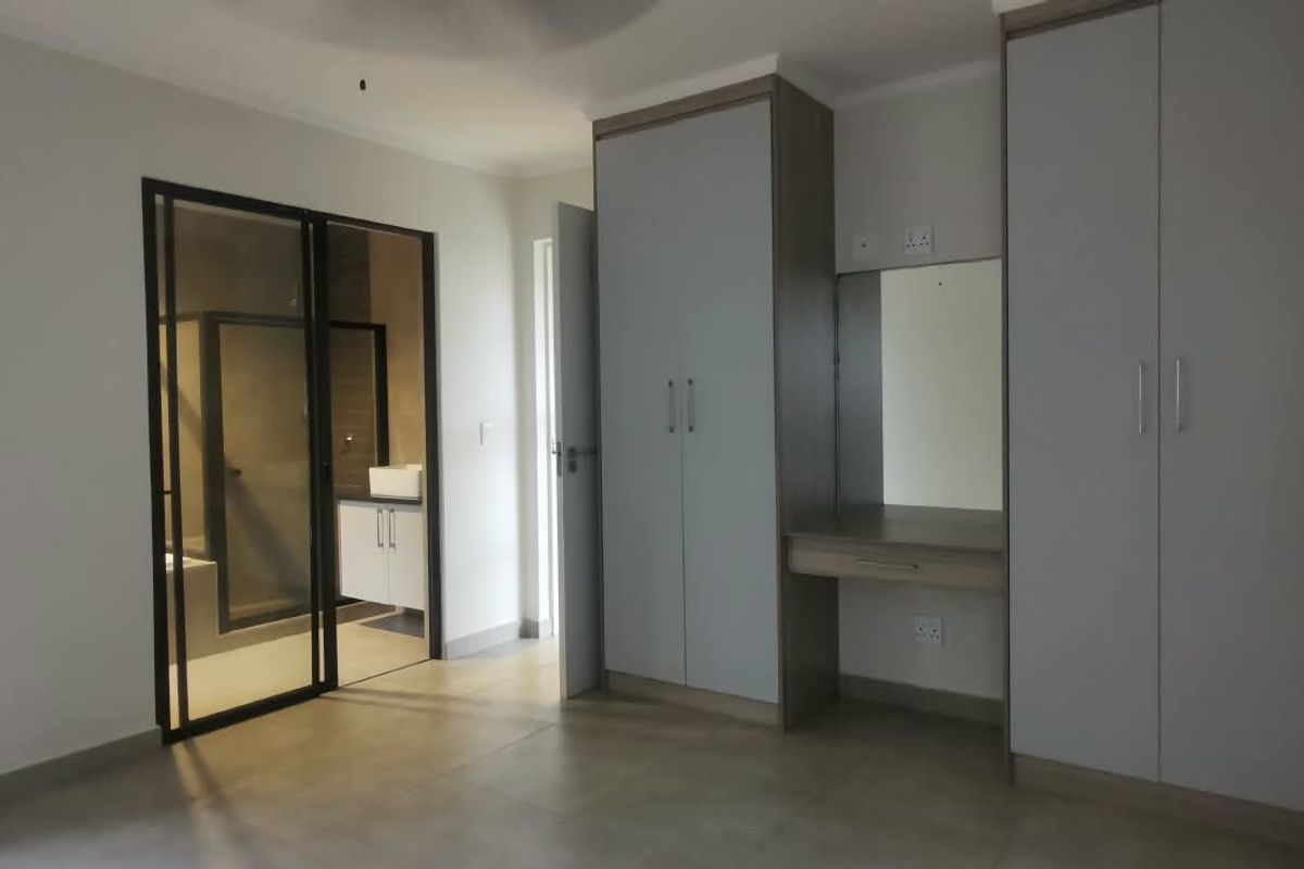 Spacious bedroom featuring modern built-in cupboards, a vanity station, tiled flooring, and direct access to an en-suite bathroom.