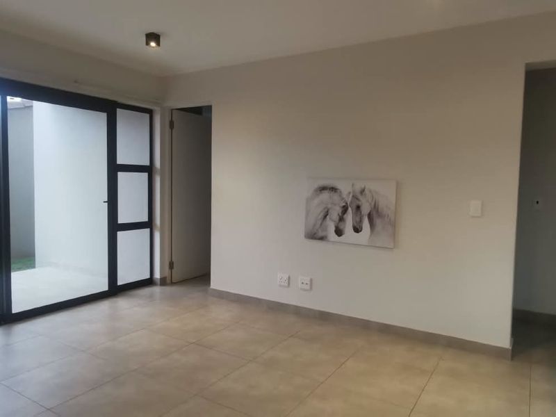 An open-plan living area featuring large sliding glass doors leading to an outdoor space, neutral tiled flooring, and modern finishes.