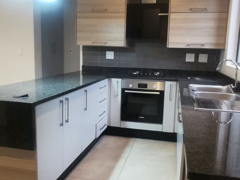 Modern kitchen featuring sleek two-tone cabinetry, granite countertops, built-in oven, gas hob, and tiled flooring in a clean, functional layout.