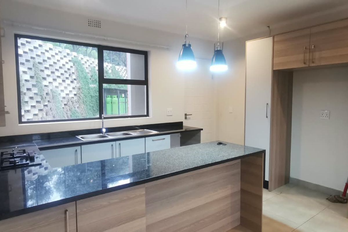Modern kitchen featuring wood-finish cabinetry, granite countertops, a gas hob, and a double sink, offering a clean and functional workspace.