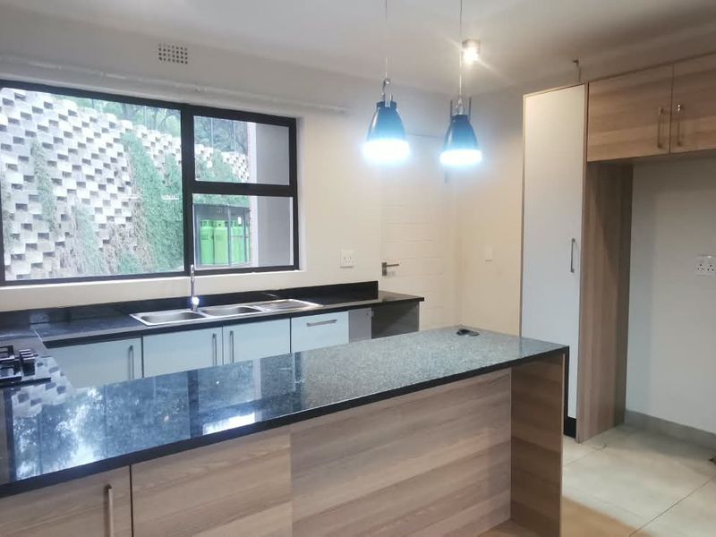 Modern kitchen featuring wood-finish cabinetry, granite countertops, a gas hob, and a double sink, offering a clean and functional workspace.