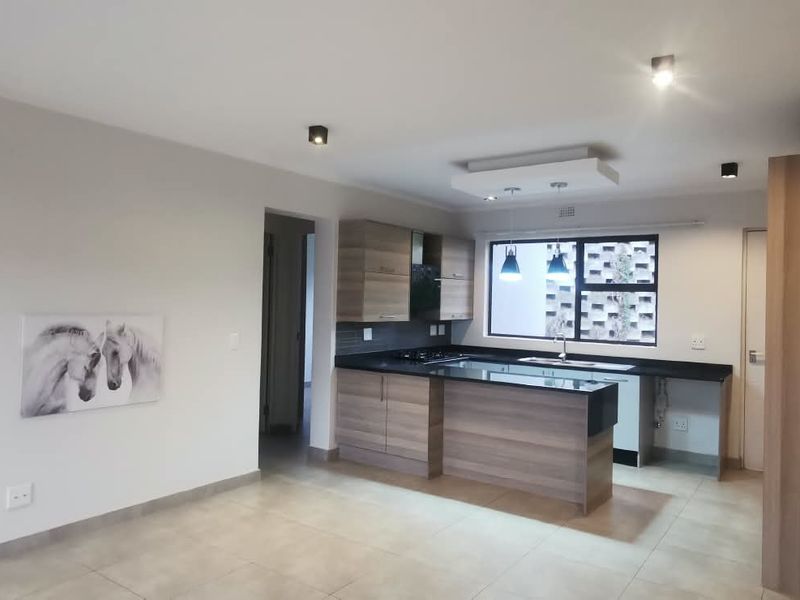 Modern open-plan kitchen and living area featuring wood-finish cabinetry, stone countertops, integrated hob, and neutral tiled flooring throughout.