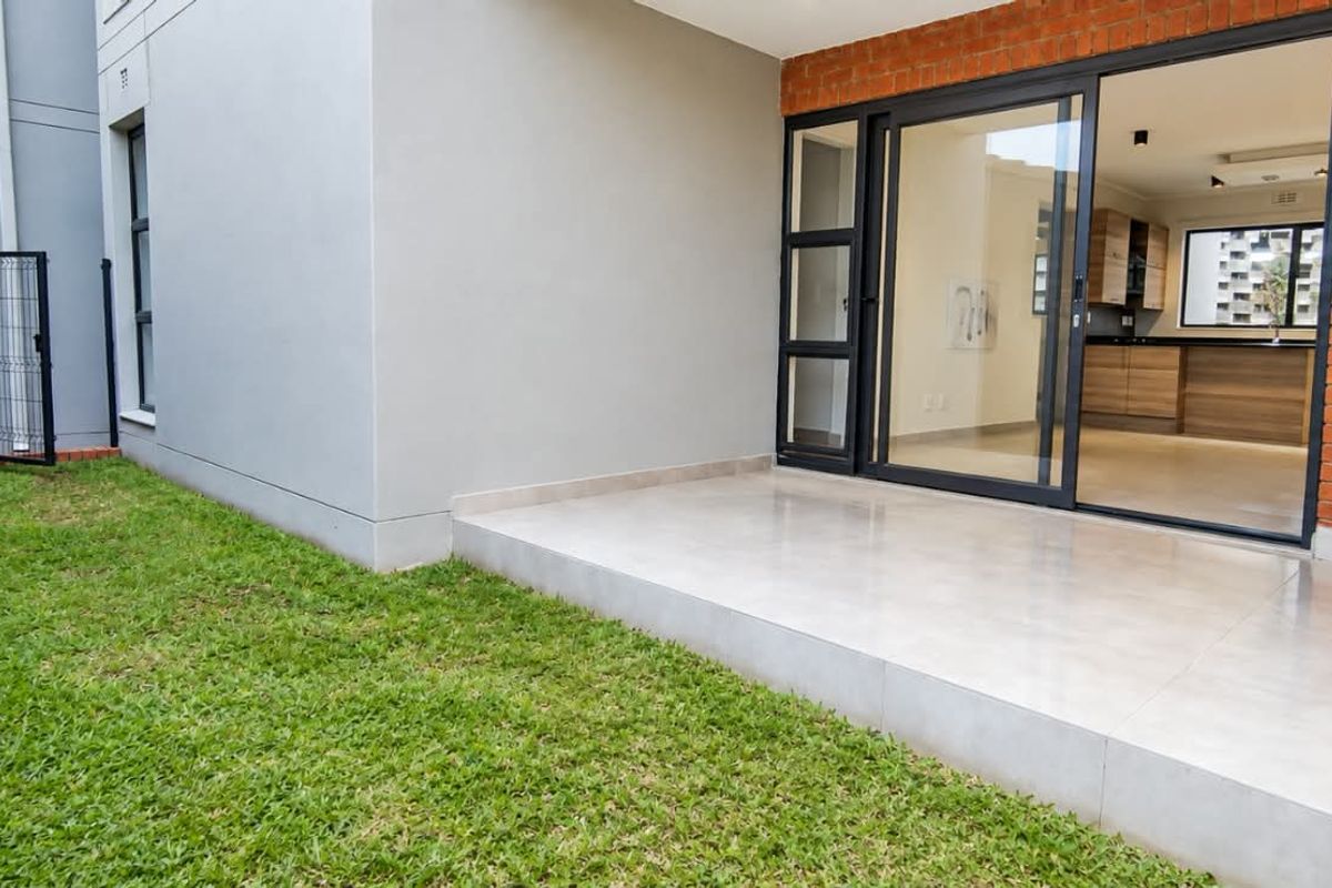 A well-maintained rear exterior featuring a tiled patio, a small private lawn, and sliding glass doors providing access to the interior living space.