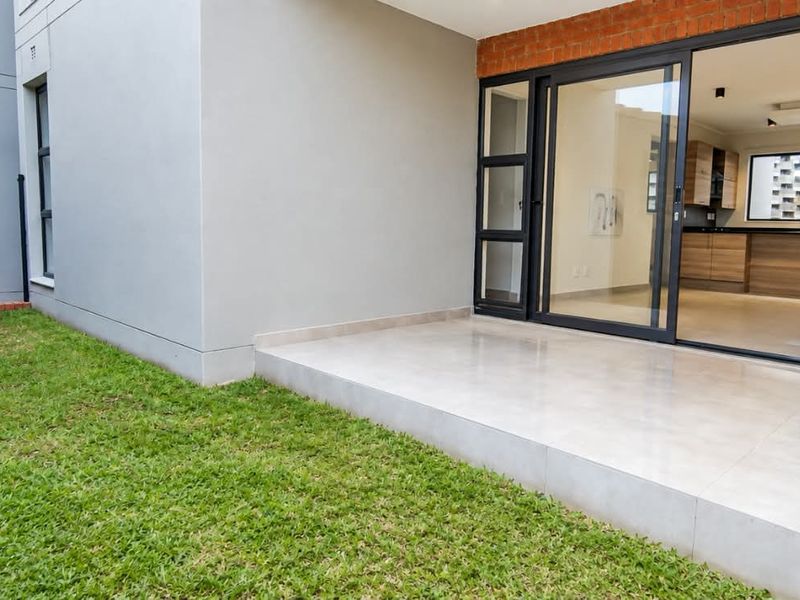 A well-maintained rear exterior featuring a tiled patio, a small private lawn, and sliding glass doors providing access to the interior living space.