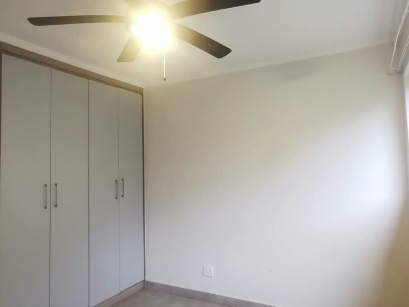 A clean, empty bedroom featuring built-in cupboards, a ceiling fan, and large windows allowing natural light.