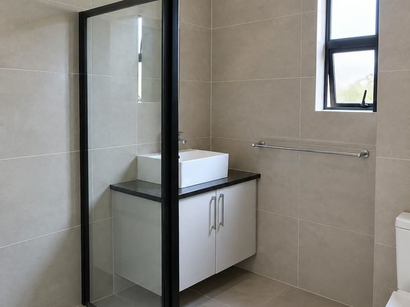 Modern bathroom featuring a walk-in shower with black-framed glass, a vanity with a vessel sink, neutral wall tiles, and an extractor fan.