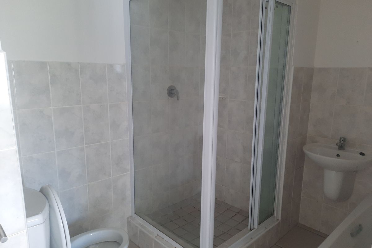 A functional bathroom featuring a shower enclosure, pedestal basin, and toilet with neutral wall and floor tiling.