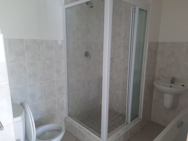 A functional bathroom featuring a shower enclosure, pedestal basin, and toilet with neutral wall and floor tiling.