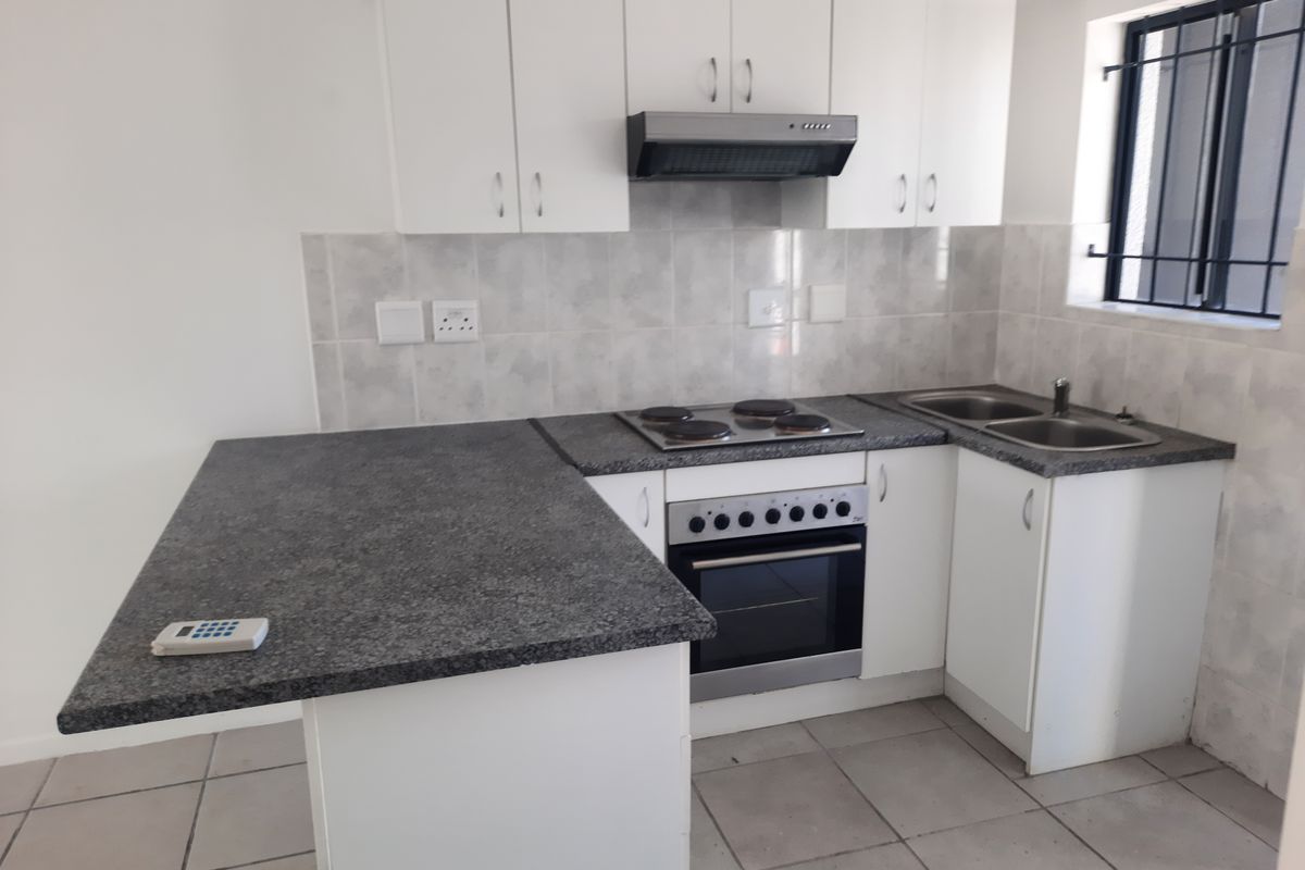 A clean, functional kitchen featuring white cabinetry, granite countertops, a built-in oven with hob, and a double sink with tiled backsplash.
