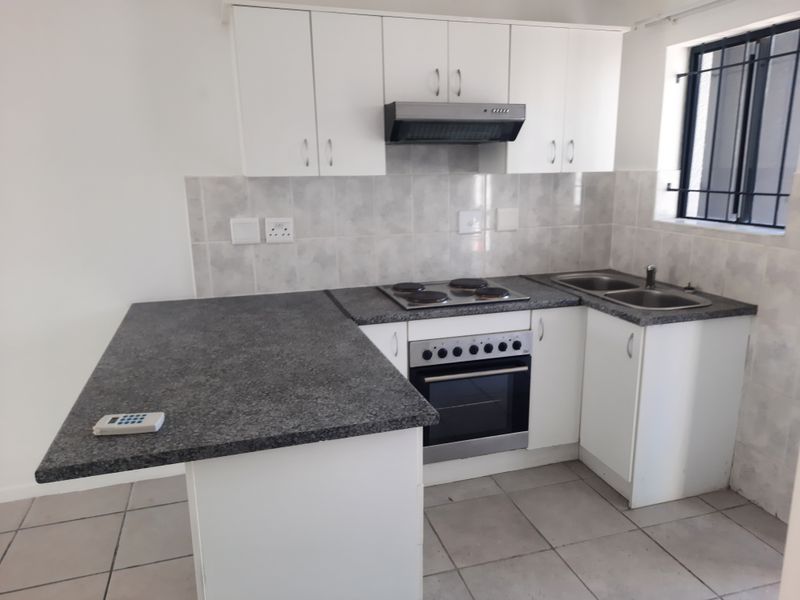 A clean, functional kitchen featuring white cabinetry, granite countertops, a built-in oven with hob, and a double sink with tiled backsplash.