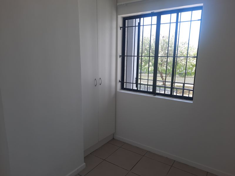 A clean, empty bedroom featuring neutral tiled flooring, built-in cupboards, and a window fitted with security bars.