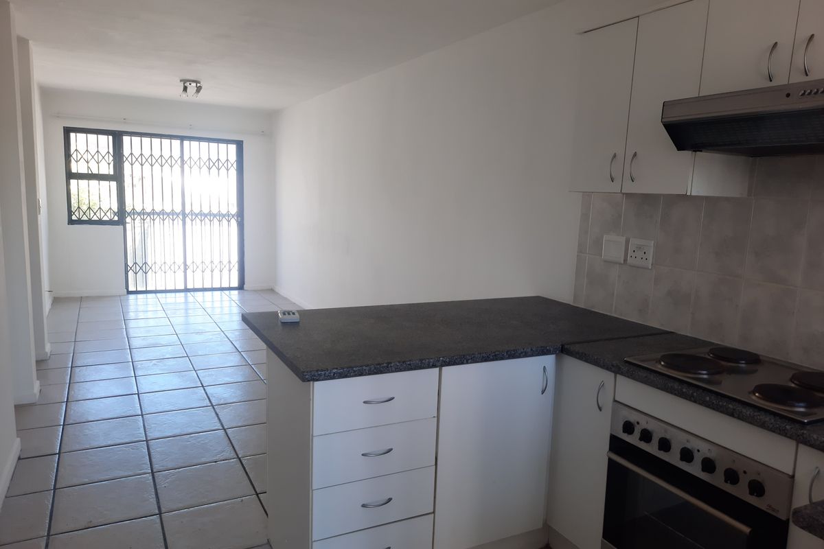 Open-plan kitchen and living area featuring tiled floors, white cabinetry, and a security gate leading to the exterior.