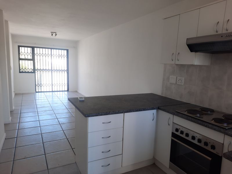 Open-plan kitchen and living area featuring tiled floors, white cabinetry, and a security gate leading to the exterior.