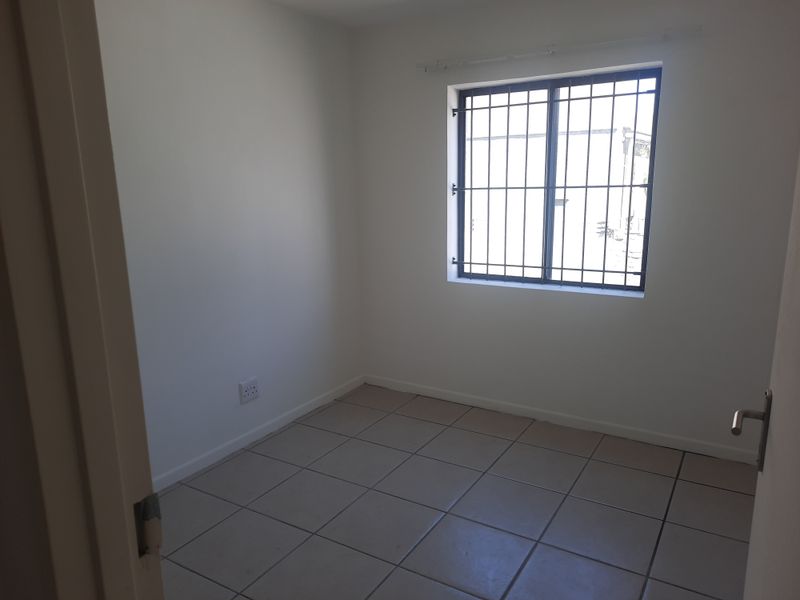 A clean, empty bedroom featuring neutral tiled flooring and a window fitted with security bars, offering a blank canvas for personalization.