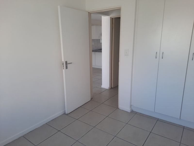 An empty bedroom featuring neutral tiled flooring and built-in cupboards, with a view through the doorway into the adjacent kitchen area.