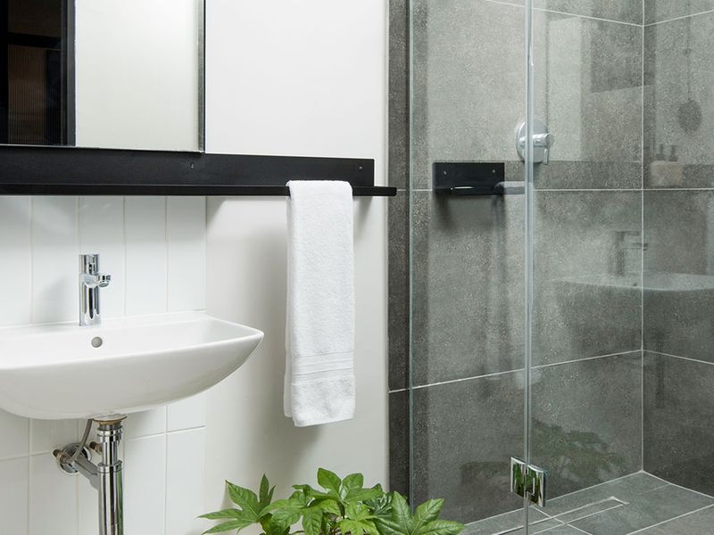 Modern bathroom featuring a wall-mounted basin, chrome fixtures, and a sleek glass-enclosed shower with contemporary grey tiling.