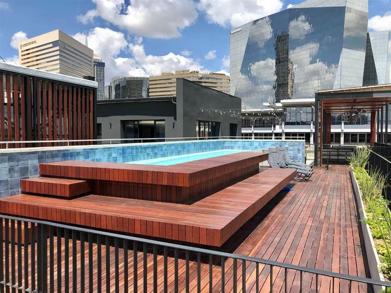 Rooftop pool area featuring raised timber decking, a tiled pool surround, and a timber pergola, set against a modern city skyline.