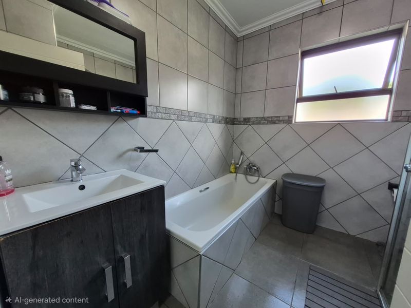 A functional bathroom featuring a built-in vanity, bathtub with mixer tap, and neutral wall and floor tiling.