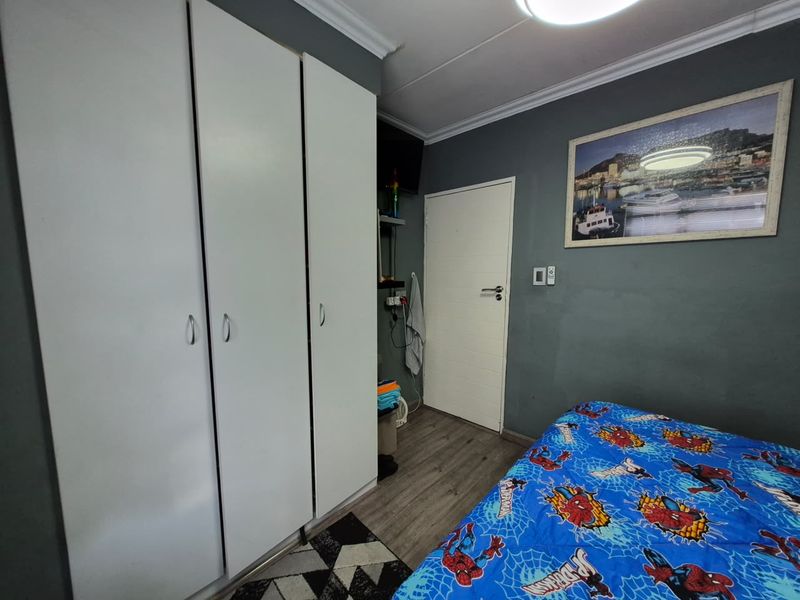 A bedroom featuring laminate flooring, built-in cupboards, and dark grey painted walls with decorative cornice detailing.