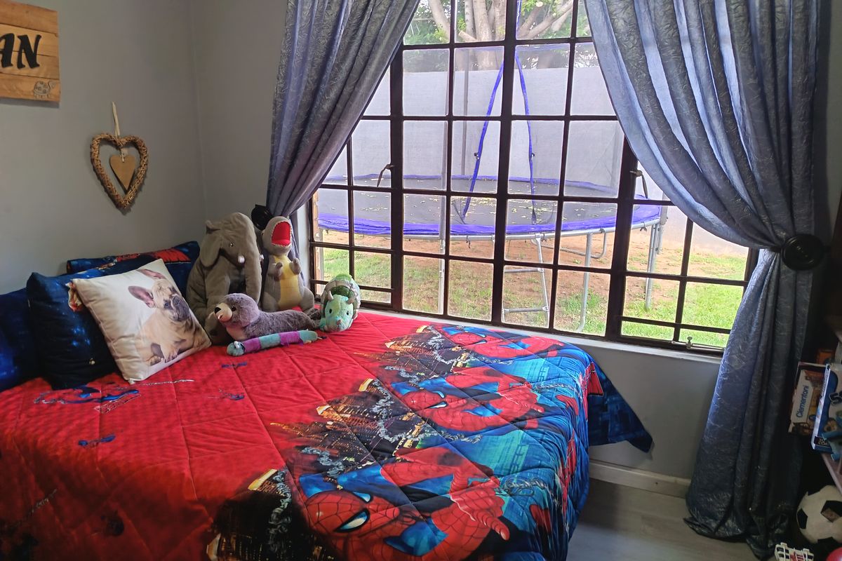A bedroom featuring laminate flooring and a large steel-framed window overlooking the garden area.