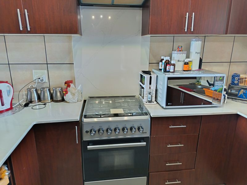A functional kitchen area featuring dark wood cabinetry, a gas stove with oven, extractor fan, and a clean stone countertop with tiled backsplash.