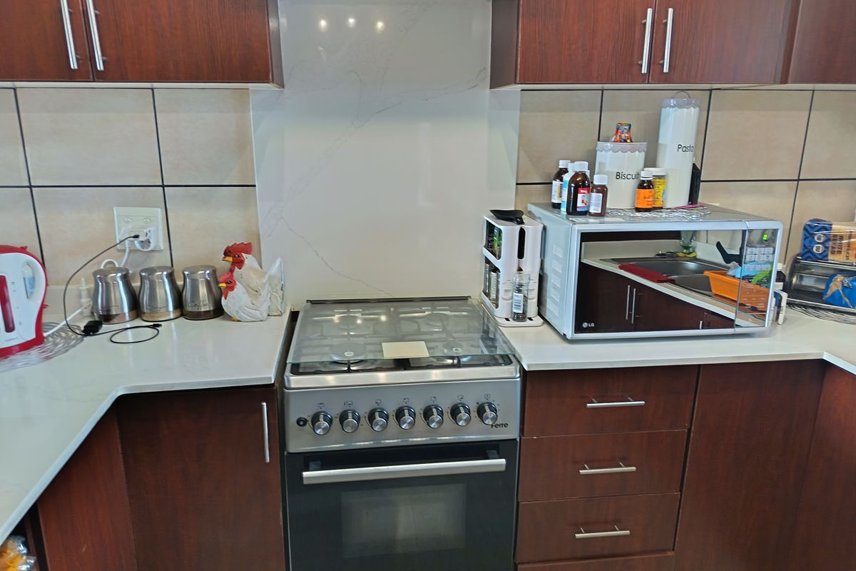 A functional kitchen area featuring dark wood cabinetry, a gas stove with oven, extractor fan, and a clean stone countertop with tiled backsplash.