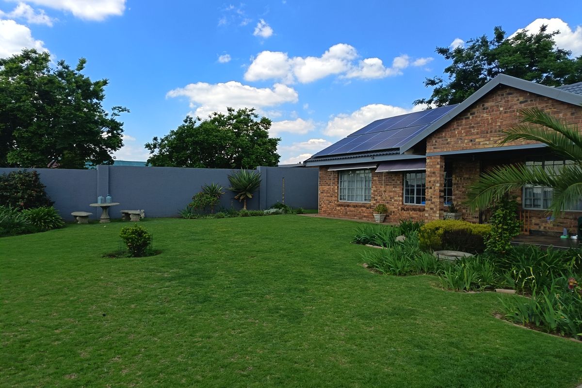 A well-maintained rear garden featuring a lush lawn, landscaped borders, and a brick-faced house equipped with roof-mounted solar panels.