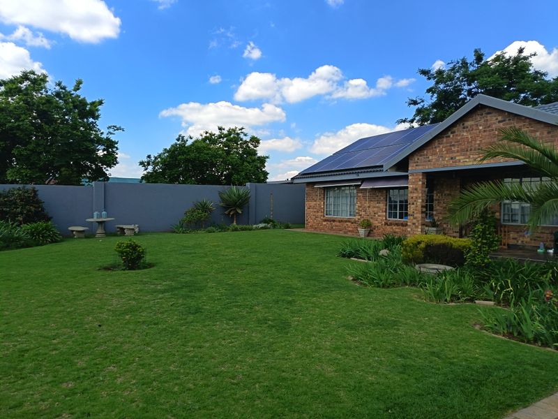 A well-maintained rear garden featuring a lush lawn, landscaped borders, and a brick-faced house equipped with roof-mounted solar panels.
