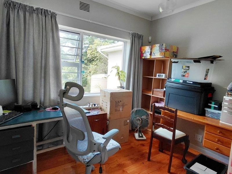 A functional home office featuring polished hardwood flooring, a built-in desk workspace, and a large window providing natural light.