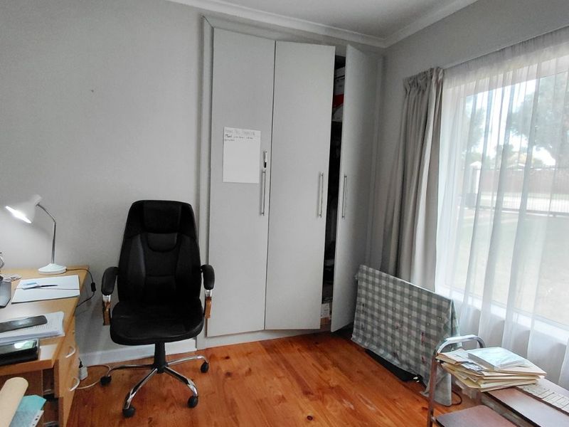 A bedroom featuring polished timber flooring, a built-in wardrobe, and large windows allowing natural light.