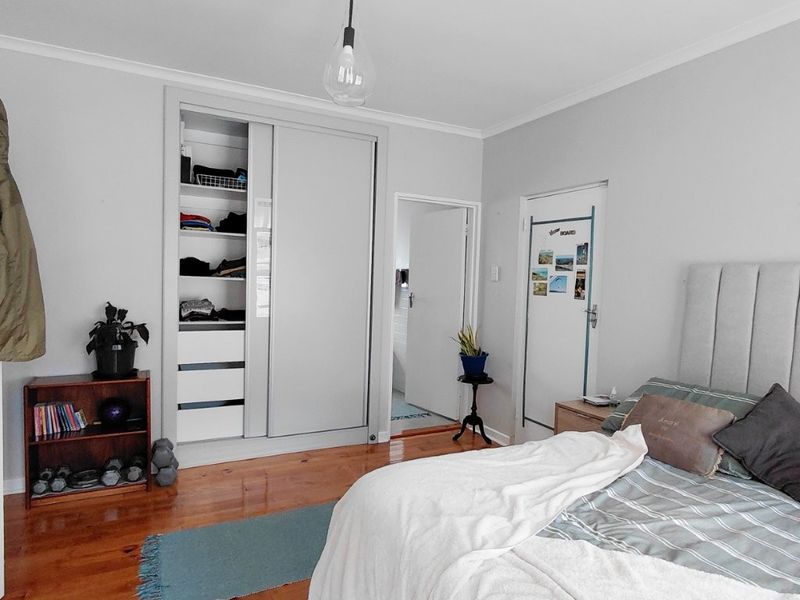 A well-maintained bedroom featuring polished hardwood flooring, a built-in sliding door wardrobe, and a modern pendant light fixture.
