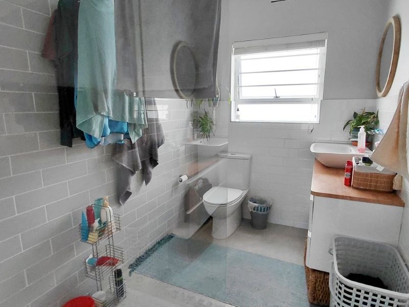 A functional bathroom featuring a glass shower screen, subway wall tiling, a modern vanity with a vessel sink, and a louvre window for ventilation.