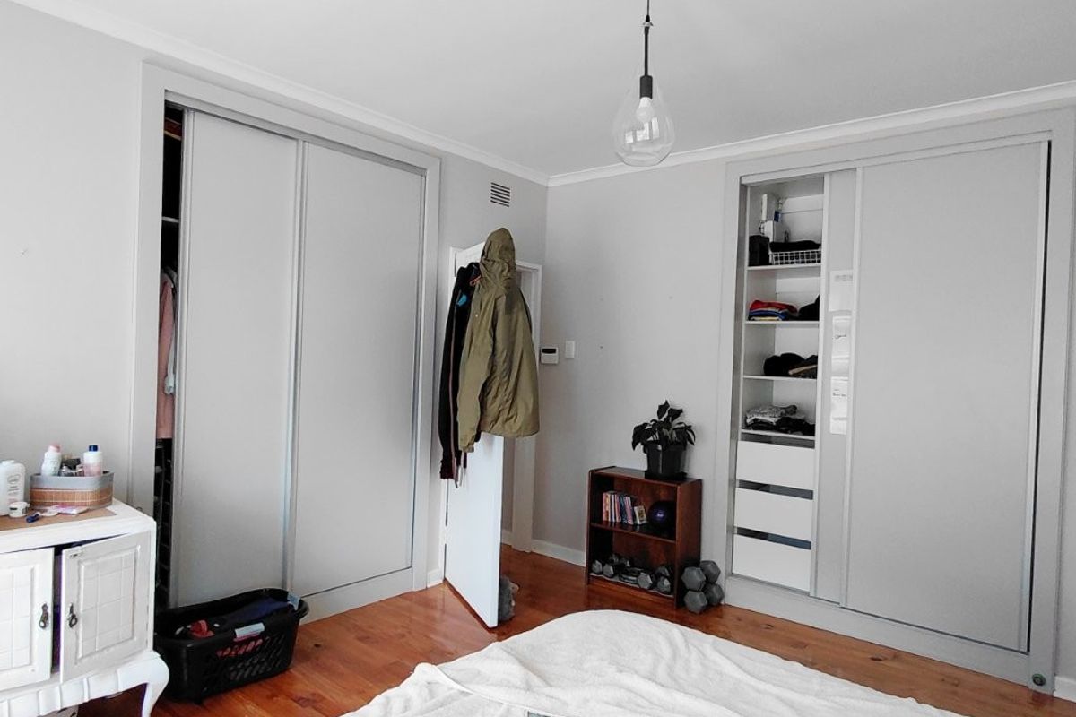 A bedroom featuring timber flooring, neutral walls, and extensive built-in cupboard storage with sliding doors.