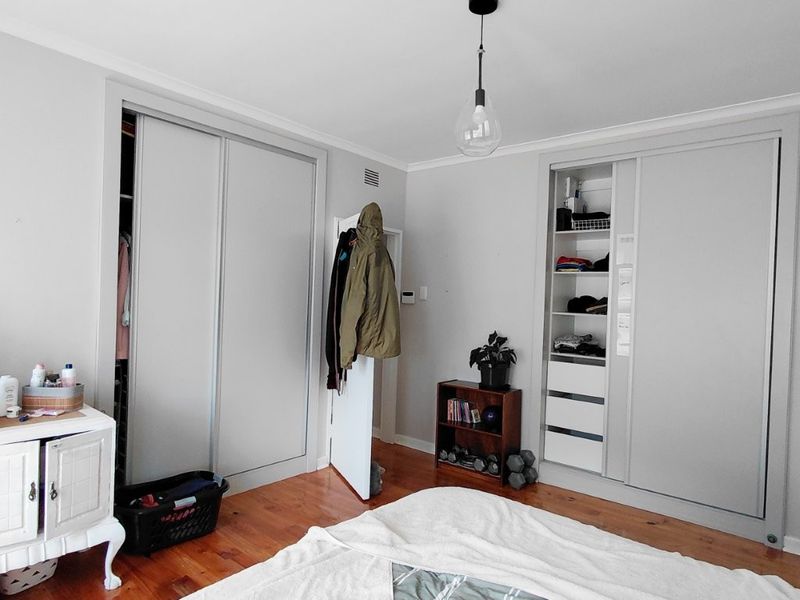 A bedroom featuring timber flooring, neutral walls, and extensive built-in cupboard storage with sliding doors.