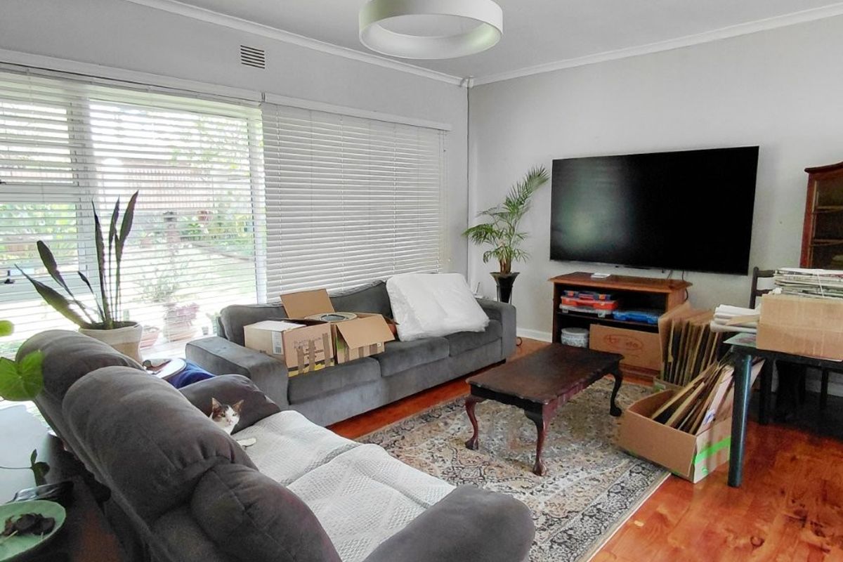 A living room featuring polished hardwood flooring, large windows with venetian blinds, and a contemporary circular pendant light fixture.