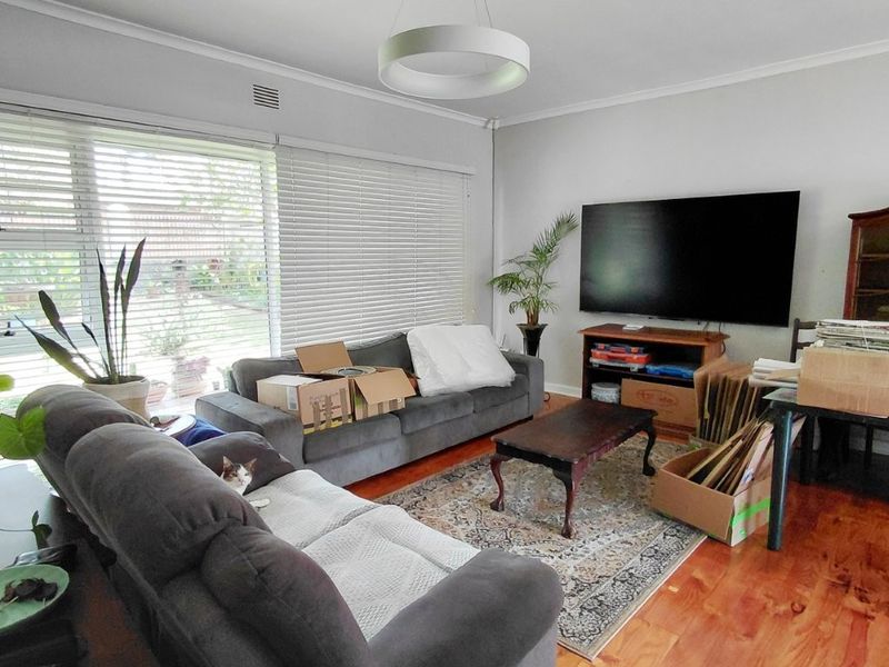A living room featuring polished hardwood flooring, large windows with venetian blinds, and a contemporary circular pendant light fixture.