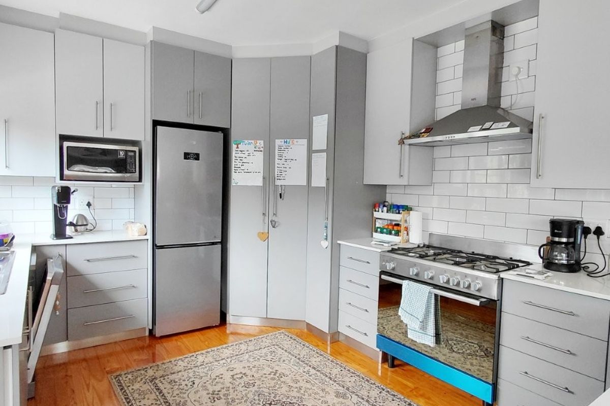 Modern kitchen featuring grey cabinetry, subway tile backsplash, stainless steel gas cooktop, oven, and extractor fan, complemented by warm hardwood flooring.