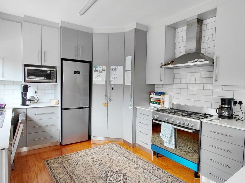 Modern kitchen featuring grey cabinetry, subway tile backsplash, stainless steel gas cooktop, oven, and extractor fan, complemented by warm hardwood flooring.