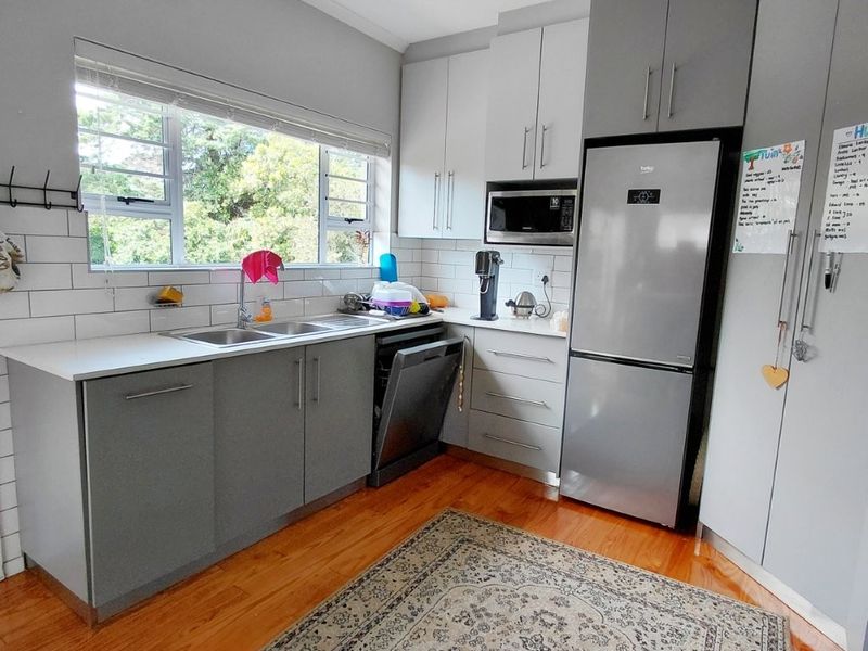 A functional kitchen featuring modern grey cabinetry, subway tile backsplash, double basin sink, and hardwood flooring with ample storage space.