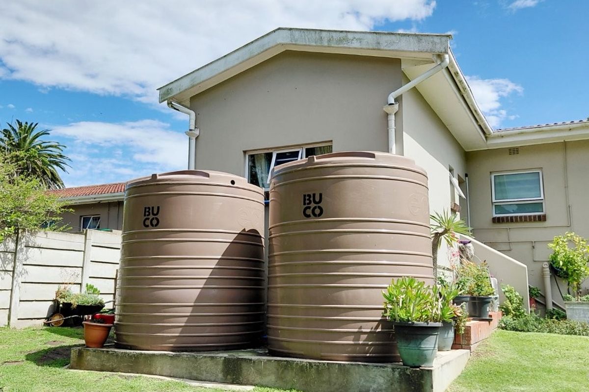 Rear exterior view of the property featuring two large water storage tanks mounted on a concrete plinth with established garden space.