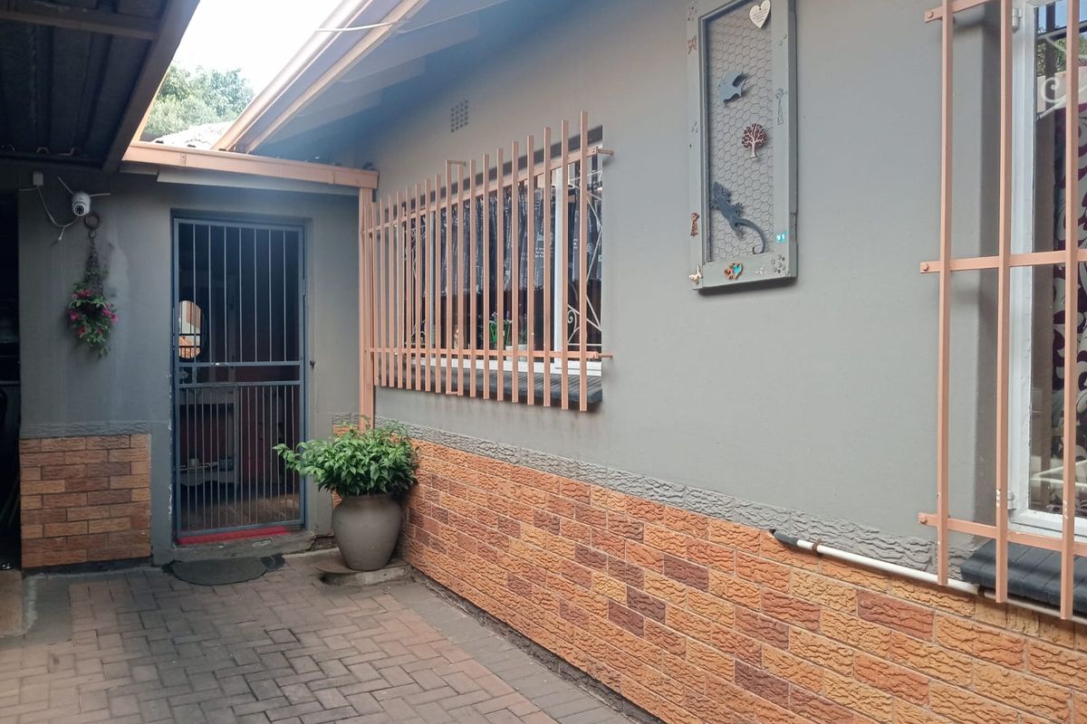 A paved rear courtyard area featuring a security gate entrance and exterior walls with brick cladding and security bars on the windows.