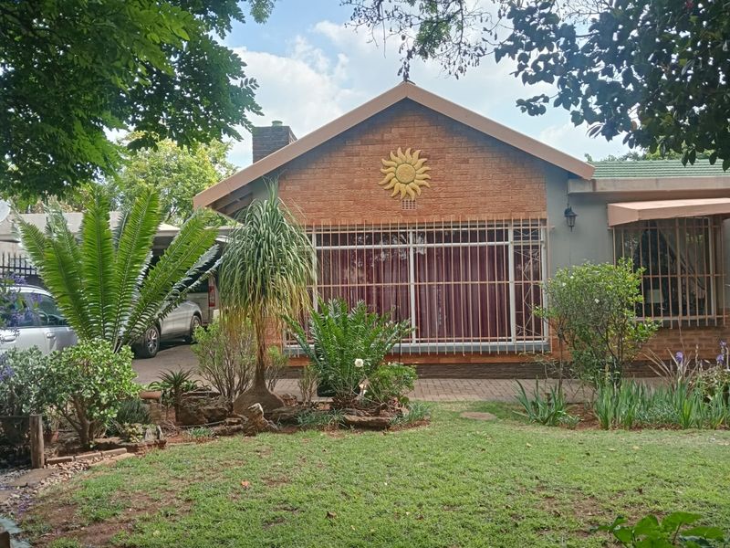 Front view of a single-story brick house featuring a paved driveway, established garden, and security bars on the windows.
