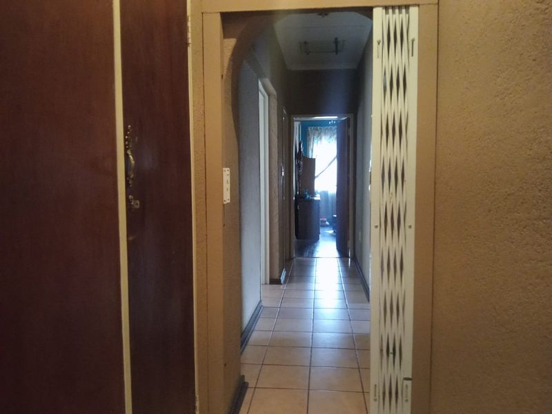 A narrow hallway featuring tiled flooring, an arched entryway, and a white security gate, leading towards a bedroom area.