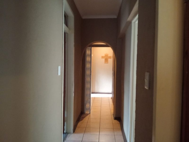 A neutral-toned hallway featuring tiled flooring and an arched doorway leading to an adjacent room.