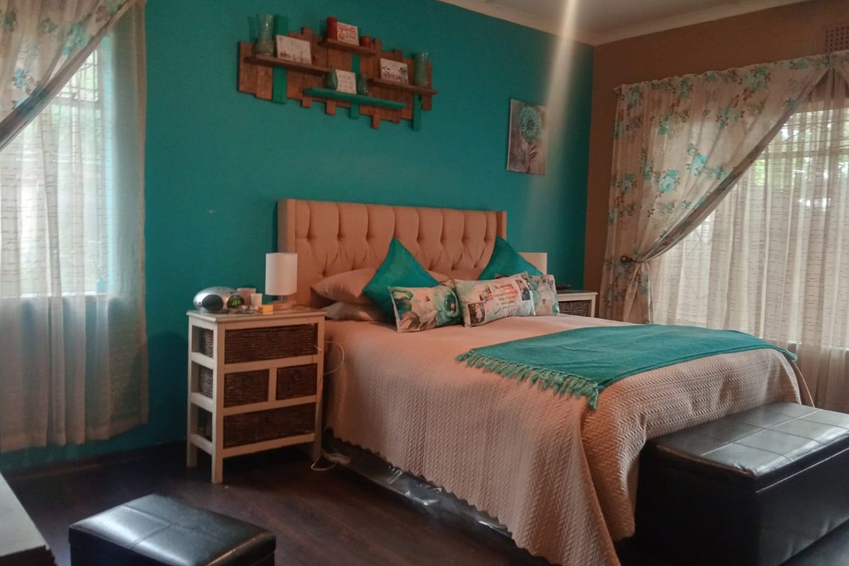 A bedroom featuring laminate flooring and a ceiling fan, with a bold teal accent wall.